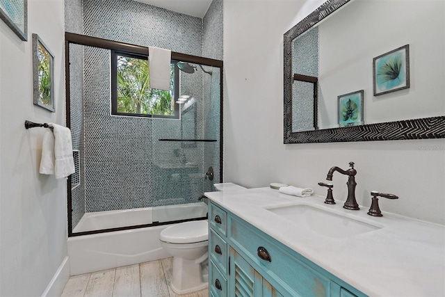 full bathroom with hardwood / wood-style flooring, combined bath / shower with glass door, vanity, and toilet