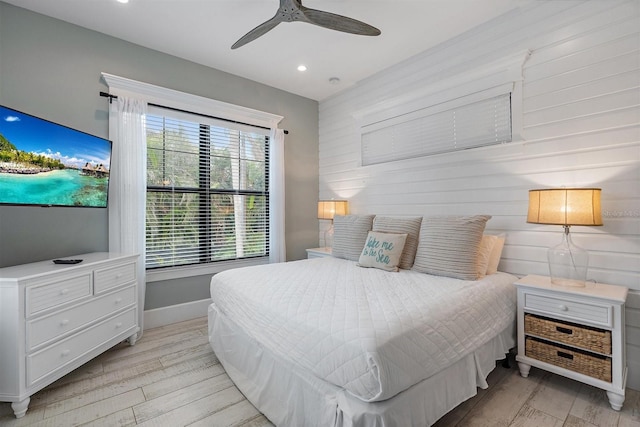 bedroom with ceiling fan, light wood-type flooring, and wood walls