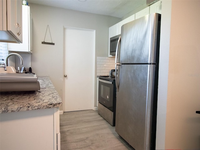 kitchen featuring white cabinets, decorative backsplash, light wood-type flooring, and appliances with stainless steel finishes