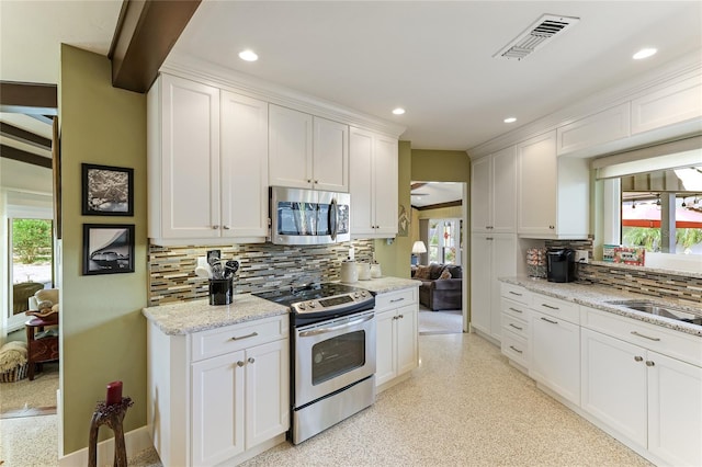 kitchen with stainless steel appliances, white cabinets, sink, backsplash, and light stone countertops