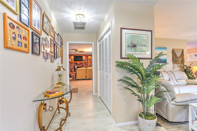 hallway with a textured ceiling and light hardwood / wood-style flooring