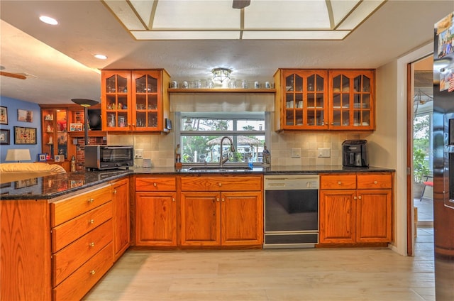 kitchen featuring light hardwood / wood-style floors, black dishwasher, sink, tasteful backsplash, and dark stone countertops