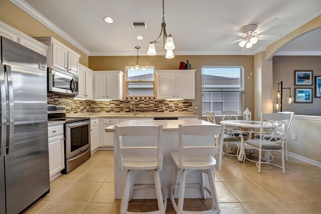 kitchen featuring stainless steel appliances, a center island, hanging light fixtures, ornamental molding, and white cabinetry