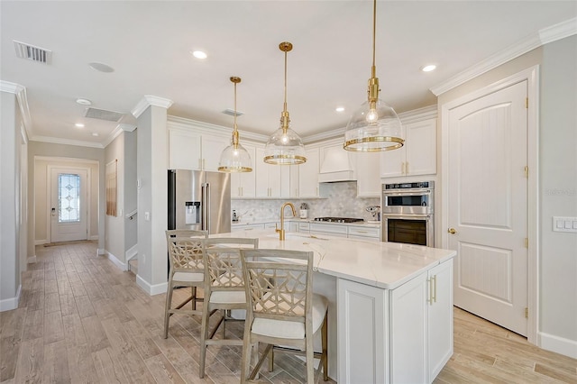 kitchen featuring appliances with stainless steel finishes, decorative light fixtures, white cabinetry, ornamental molding, and a center island with sink