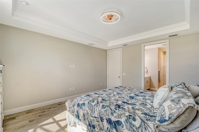 bedroom featuring crown molding, light hardwood / wood-style floors, a raised ceiling, and ensuite bathroom