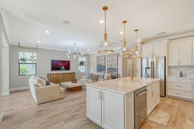 kitchen featuring sink, decorative light fixtures, appliances with stainless steel finishes, an island with sink, and light stone countertops