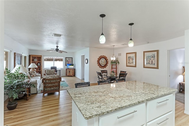 kitchen with a center island, white cabinets, hanging light fixtures, ceiling fan, and light wood-type flooring