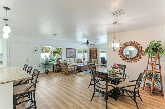 dining space featuring ceiling fan with notable chandelier, a textured ceiling, and light wood-type flooring