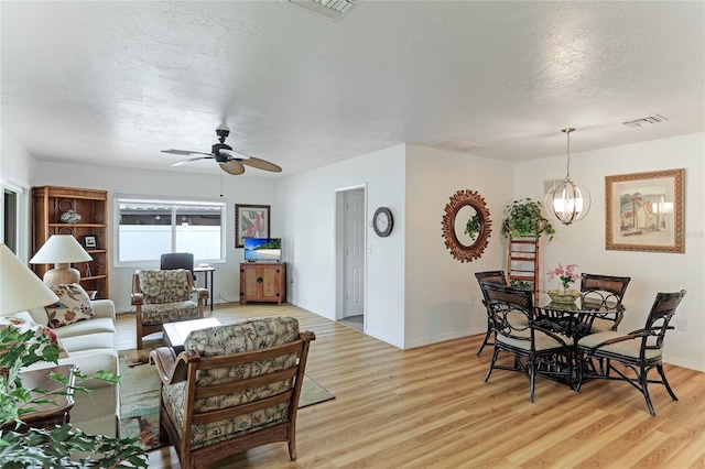 living room with ceiling fan with notable chandelier, light hardwood / wood-style flooring, and a textured ceiling