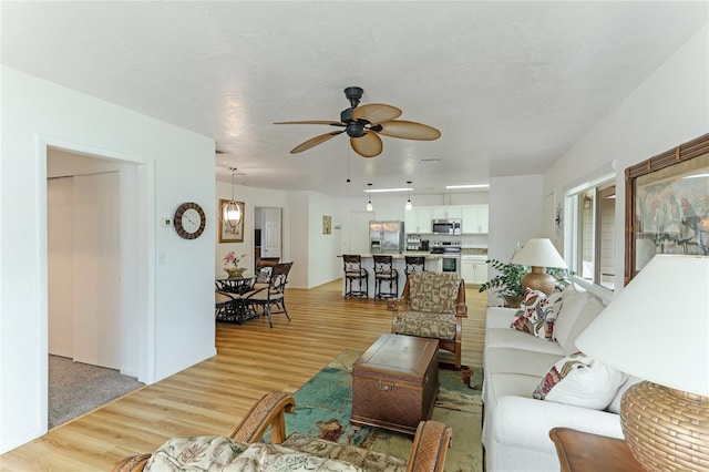 living room featuring light hardwood / wood-style floors, ceiling fan, and a textured ceiling