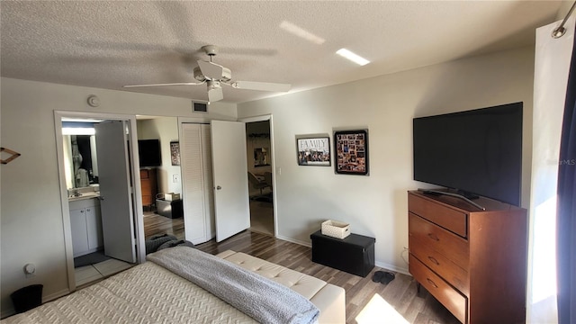 bedroom featuring a closet, ensuite bath, a textured ceiling, ceiling fan, and light hardwood / wood-style flooring