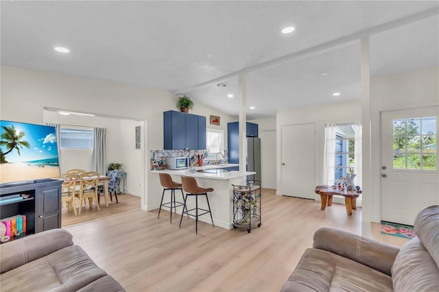 living room with sink, light wood-type flooring, and vaulted ceiling