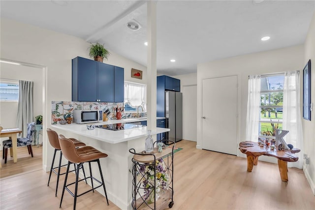 kitchen with stainless steel appliances, blue cabinetry, a kitchen bar, vaulted ceiling, and kitchen peninsula