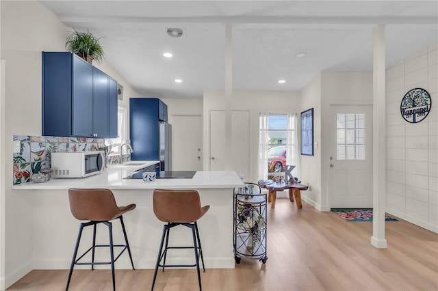 kitchen featuring sink, kitchen peninsula, a kitchen bar, blue cabinets, and light wood-type flooring