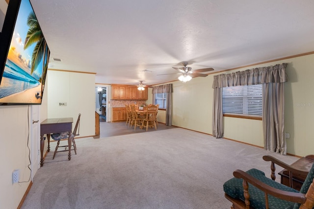 unfurnished living room featuring baseboards, light colored carpet, ornamental molding, and a ceiling fan