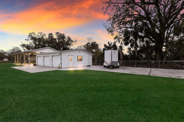 rear view of property featuring concrete driveway, a yard, fence, and an outbuilding