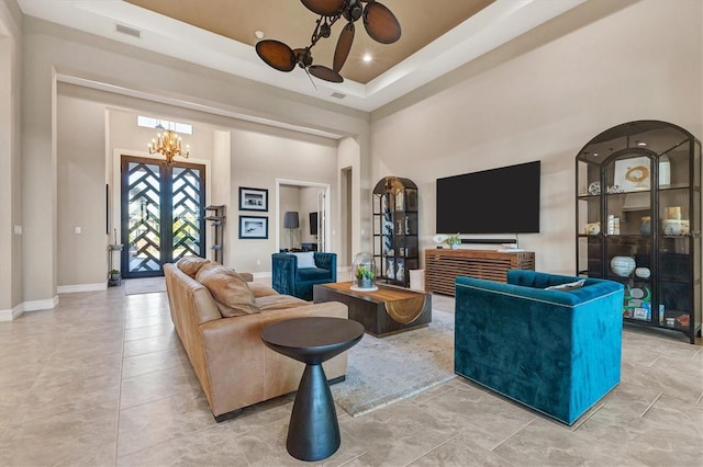 living room with a towering ceiling, ceiling fan with notable chandelier, a raised ceiling, and light tile patterned flooring