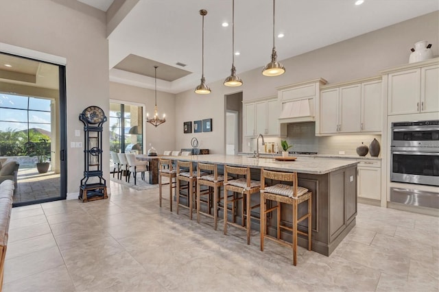 kitchen featuring a center island with sink, light stone countertops, a kitchen bar, decorative light fixtures, and double oven