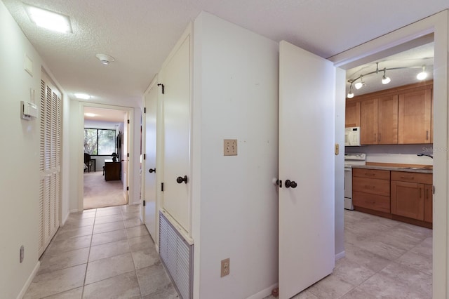 corridor with a textured ceiling, sink, and light tile patterned floors