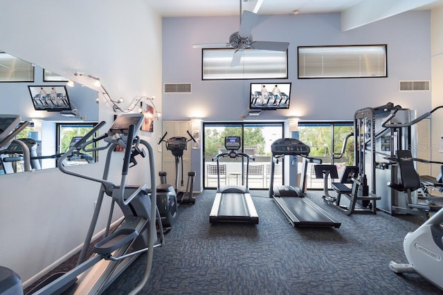 exercise room with a towering ceiling, ceiling fan, and dark colored carpet