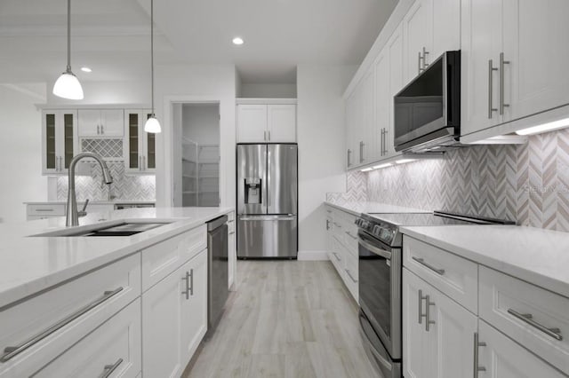 kitchen featuring stainless steel appliances, white cabinetry, sink, hanging light fixtures, and light wood-type flooring