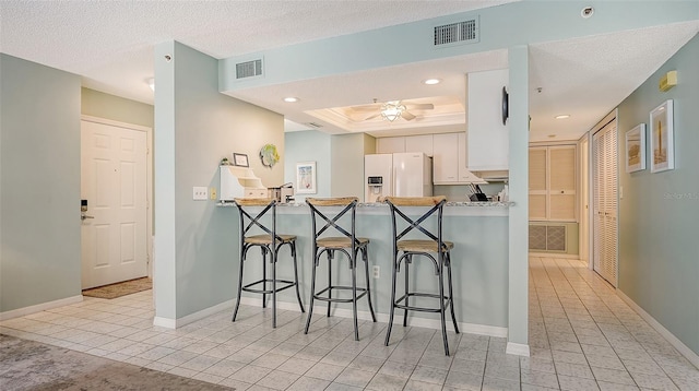 kitchen featuring a breakfast bar, kitchen peninsula, a textured ceiling, white refrigerator with ice dispenser, and white cabinets