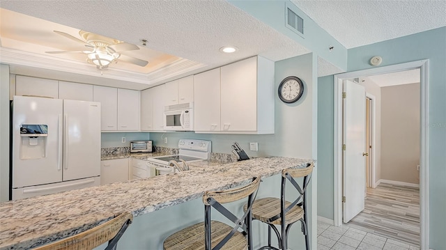 kitchen featuring light hardwood / wood-style floors, kitchen peninsula, a breakfast bar, white cabinetry, and white appliances