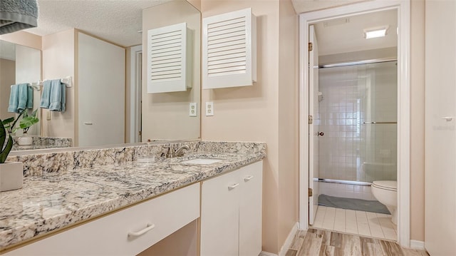 bathroom with a shower with shower door, vanity, toilet, and a textured ceiling