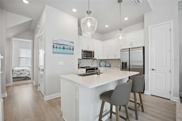 kitchen featuring light hardwood / wood-style flooring, tasteful backsplash, white cabinetry, appliances with stainless steel finishes, and decorative light fixtures