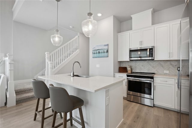 kitchen with a center island with sink, white cabinets, sink, pendant lighting, and appliances with stainless steel finishes