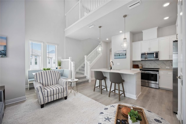 kitchen with stainless steel appliances, white cabinets, an island with sink, pendant lighting, and light wood-type flooring