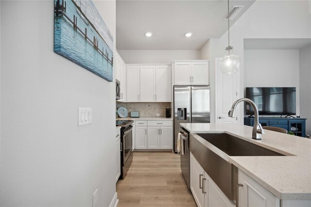 kitchen with light hardwood / wood-style flooring, hanging light fixtures, backsplash, white cabinetry, and appliances with stainless steel finishes