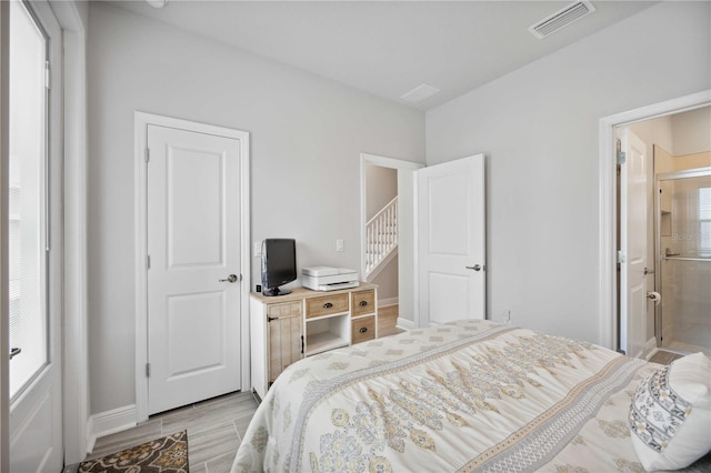 bedroom with connected bathroom, light wood-type flooring, and multiple windows