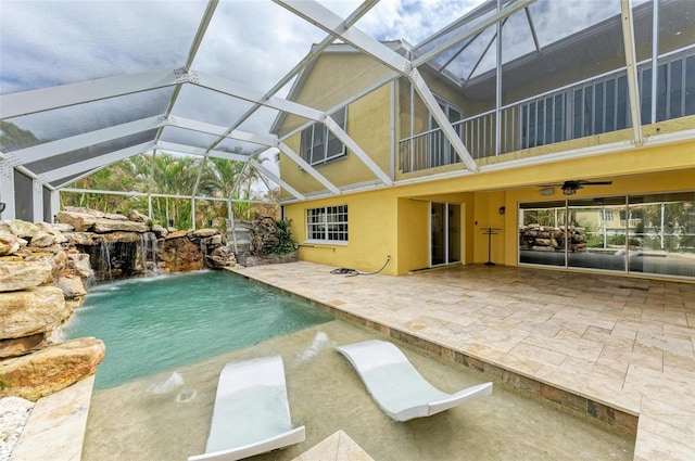 view of pool with pool water feature, a patio, glass enclosure, and ceiling fan