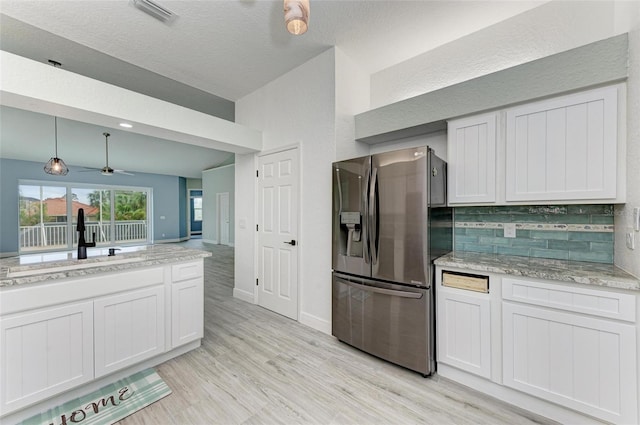 kitchen with stainless steel refrigerator with ice dispenser, white cabinetry, decorative backsplash, sink, and hanging light fixtures