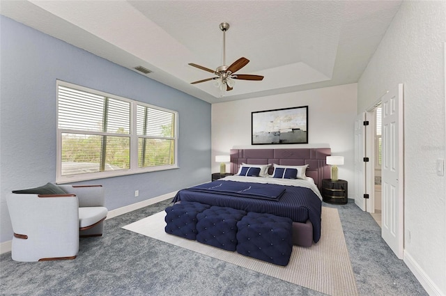 carpeted bedroom with ceiling fan, a textured ceiling, and a tray ceiling