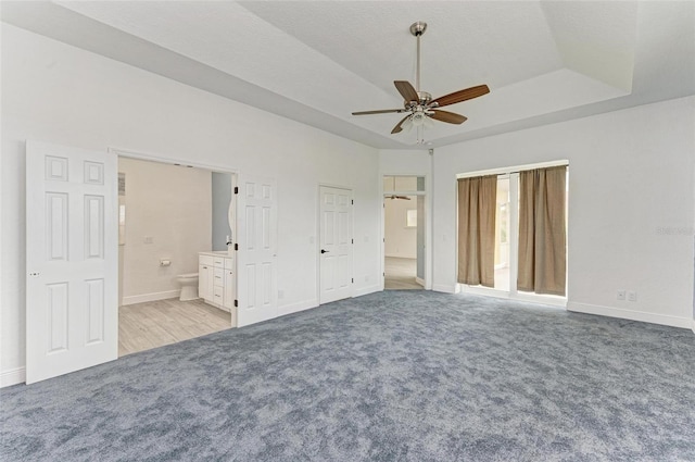 unfurnished bedroom with ceiling fan, ensuite bathroom, light colored carpet, and a tray ceiling