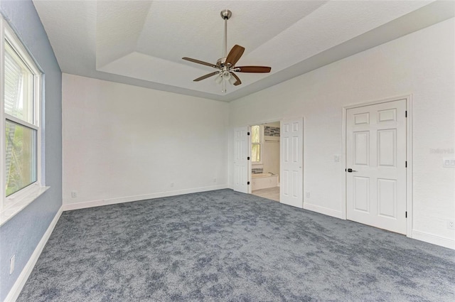 unfurnished bedroom with dark carpet, a textured ceiling, ceiling fan, and a raised ceiling