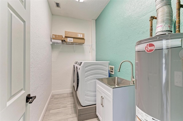 laundry area with light hardwood / wood-style flooring, washing machine and clothes dryer, cabinets, a textured ceiling, and water heater