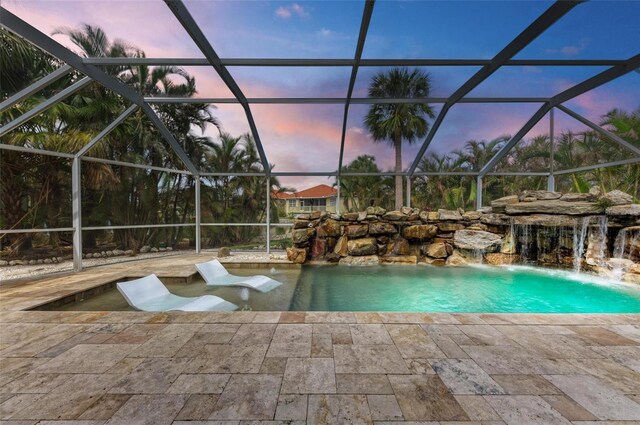 pool at dusk featuring pool water feature, glass enclosure, and a patio area