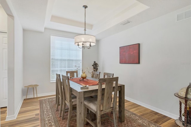 dining space featuring light hardwood / wood-style floors, a notable chandelier, a healthy amount of sunlight, and a tray ceiling