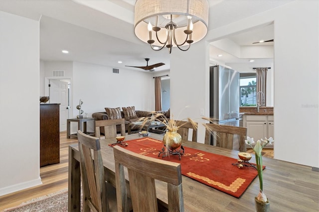 dining space featuring ceiling fan with notable chandelier, light hardwood / wood-style floors, and sink