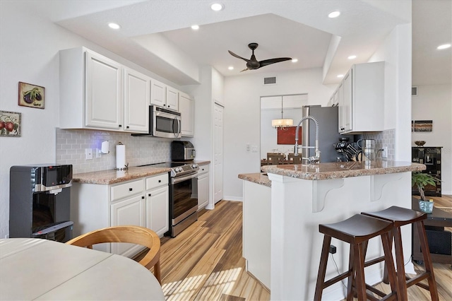 kitchen featuring light stone countertops, white cabinetry, light hardwood / wood-style floors, and appliances with stainless steel finishes