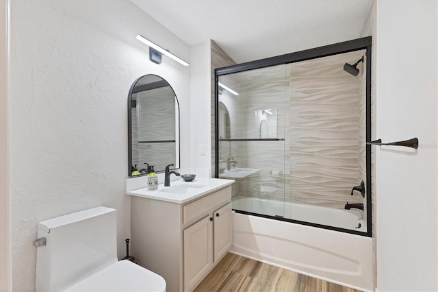 full bathroom featuring wood-type flooring, toilet, bath / shower combo with glass door, a textured ceiling, and vanity