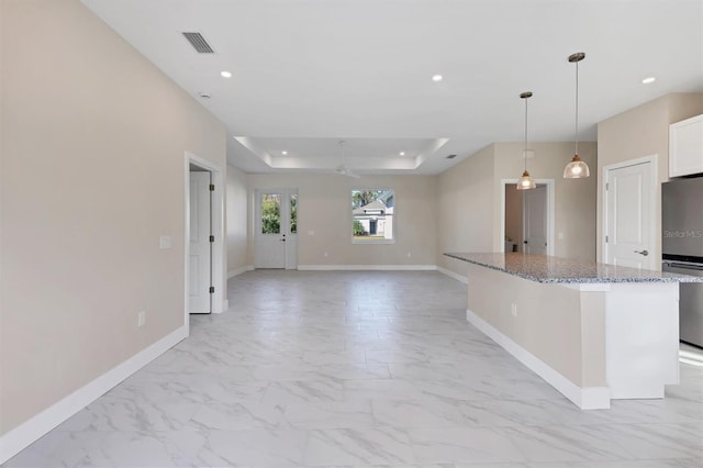 kitchen with light stone counters, a tray ceiling, ceiling fan, decorative light fixtures, and stainless steel refrigerator