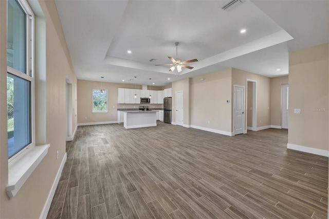 unfurnished living room featuring hardwood / wood-style floors, ceiling fan, and a raised ceiling