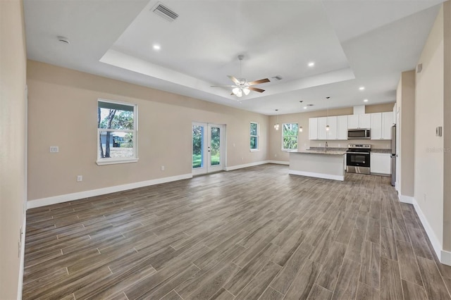 unfurnished living room featuring ceiling fan, a tray ceiling, hardwood / wood-style floors, and a healthy amount of sunlight