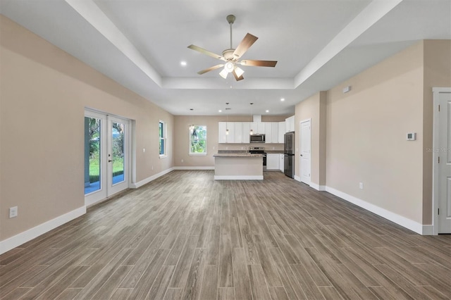 unfurnished living room featuring hardwood / wood-style floors, ceiling fan, and a raised ceiling