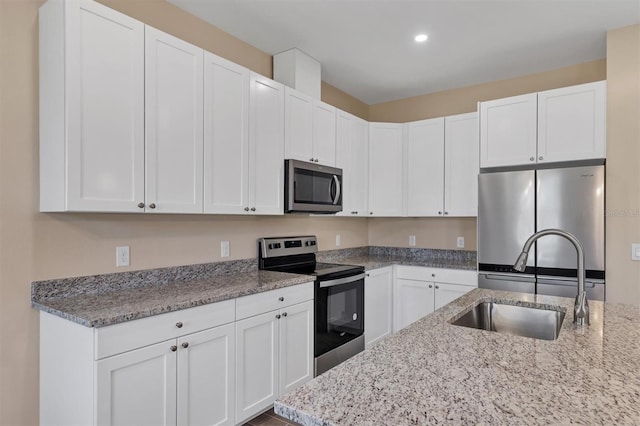 kitchen with white cabinetry, sink, light stone countertops, and stainless steel appliances