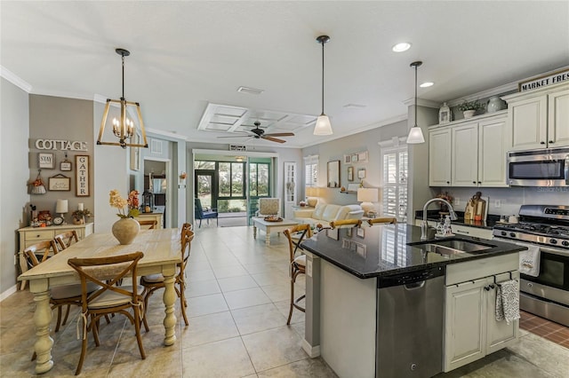 kitchen featuring ceiling fan with notable chandelier, a center island with sink, sink, ornamental molding, and appliances with stainless steel finishes